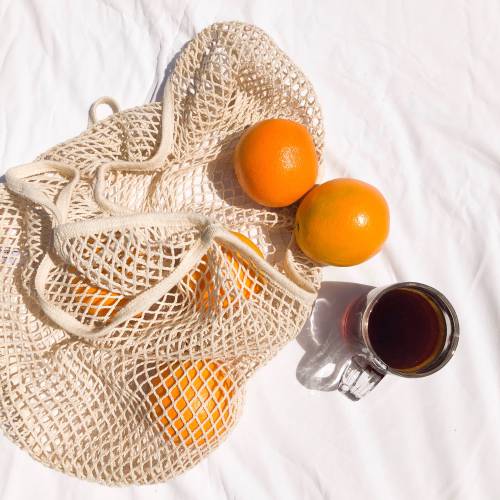 a resuable cotton bag with oranges and a black coffee in the sun 